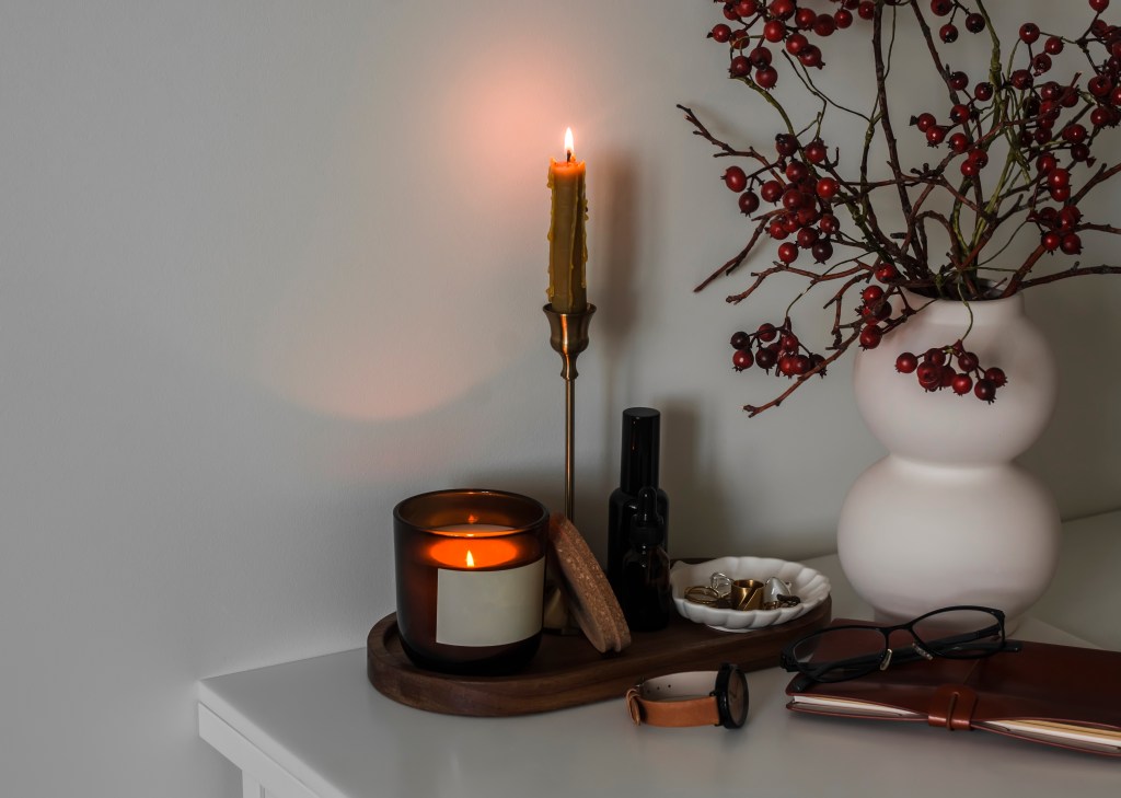 Women's bedside table with candles, ornaments, cranberry branches in a ceramic vase, notepad